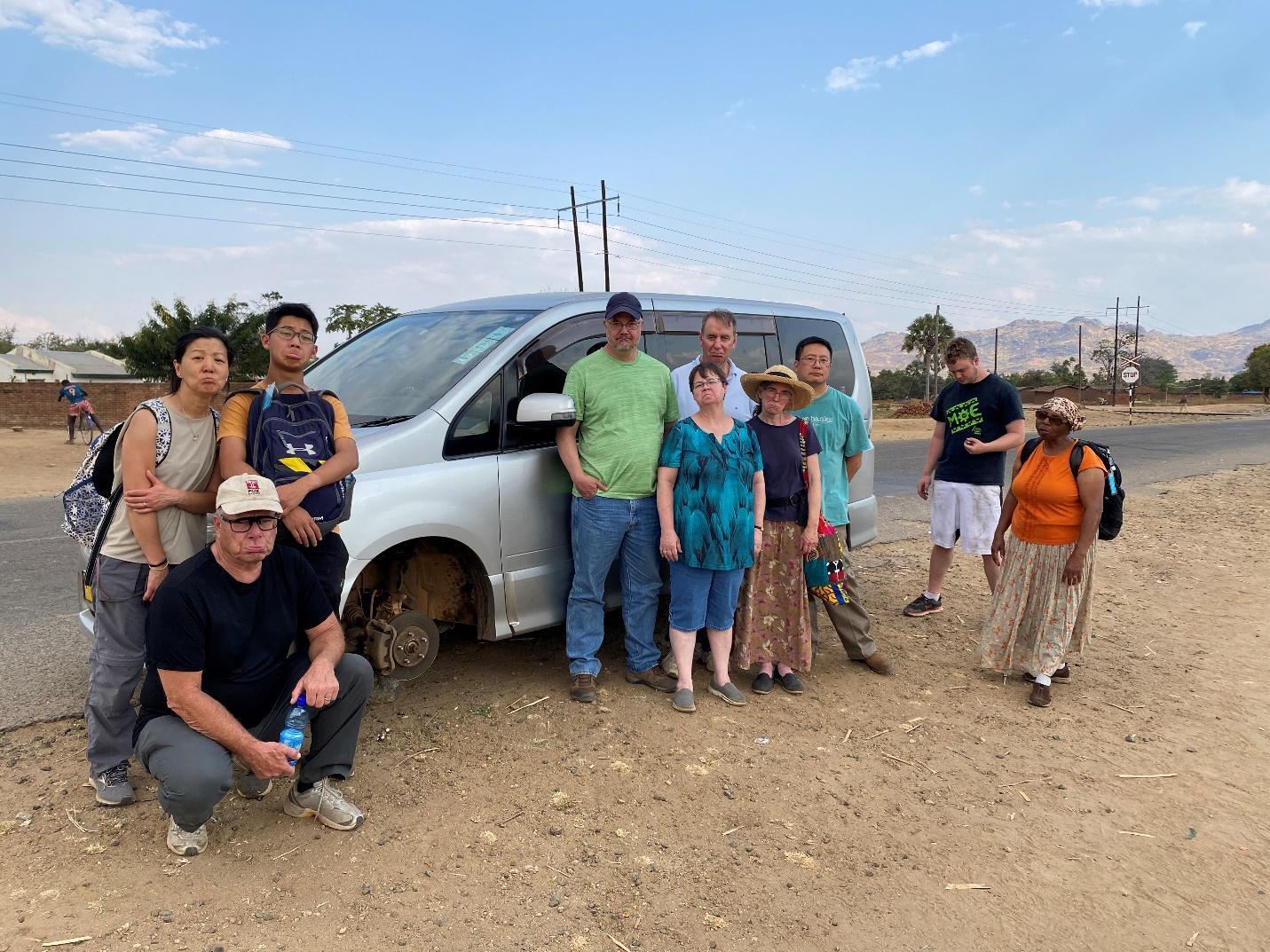 A group of people standing next to a car

Description automatically generated