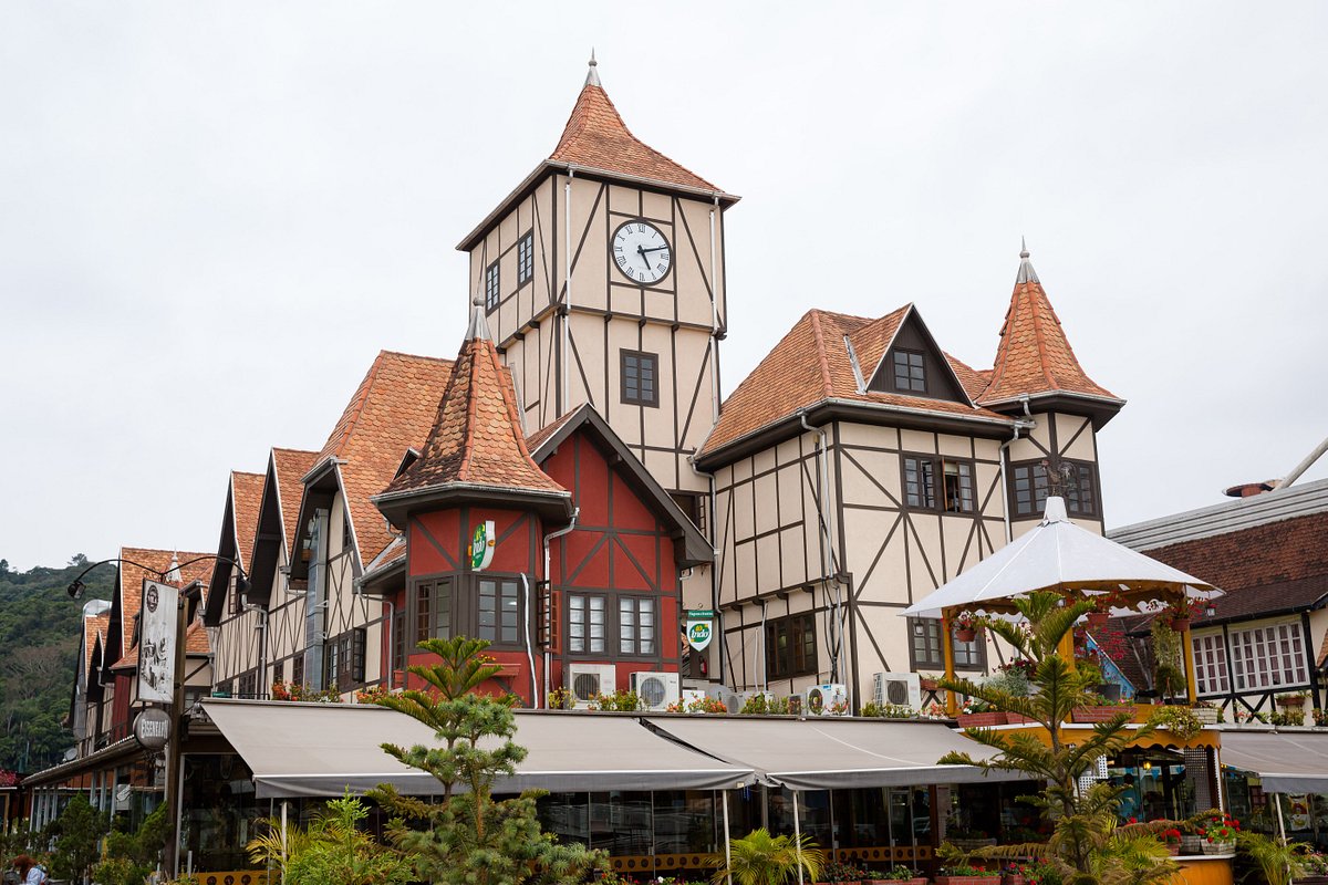 Blumenau. Foto de uma construção dentro da Vila Germânica, uma grande torre bege no meio, com um relógio no meio, seguido de casinhas menores que formam uma só construção.