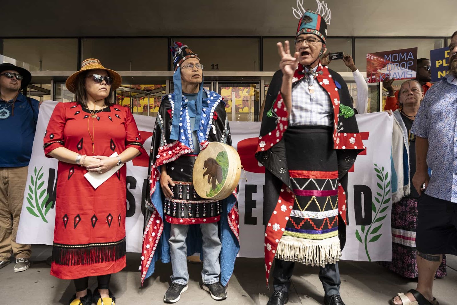 Three indigenous protesters in traditional dress address an unseen crowd