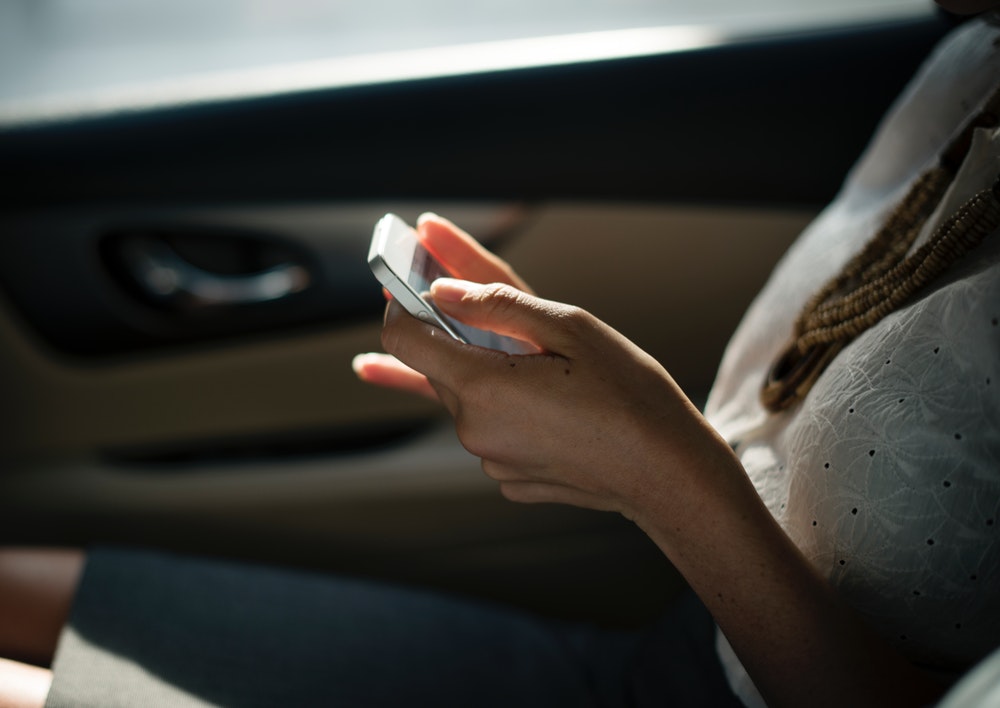 Woman sitting in car in the sunlight with a smartphone in her hands