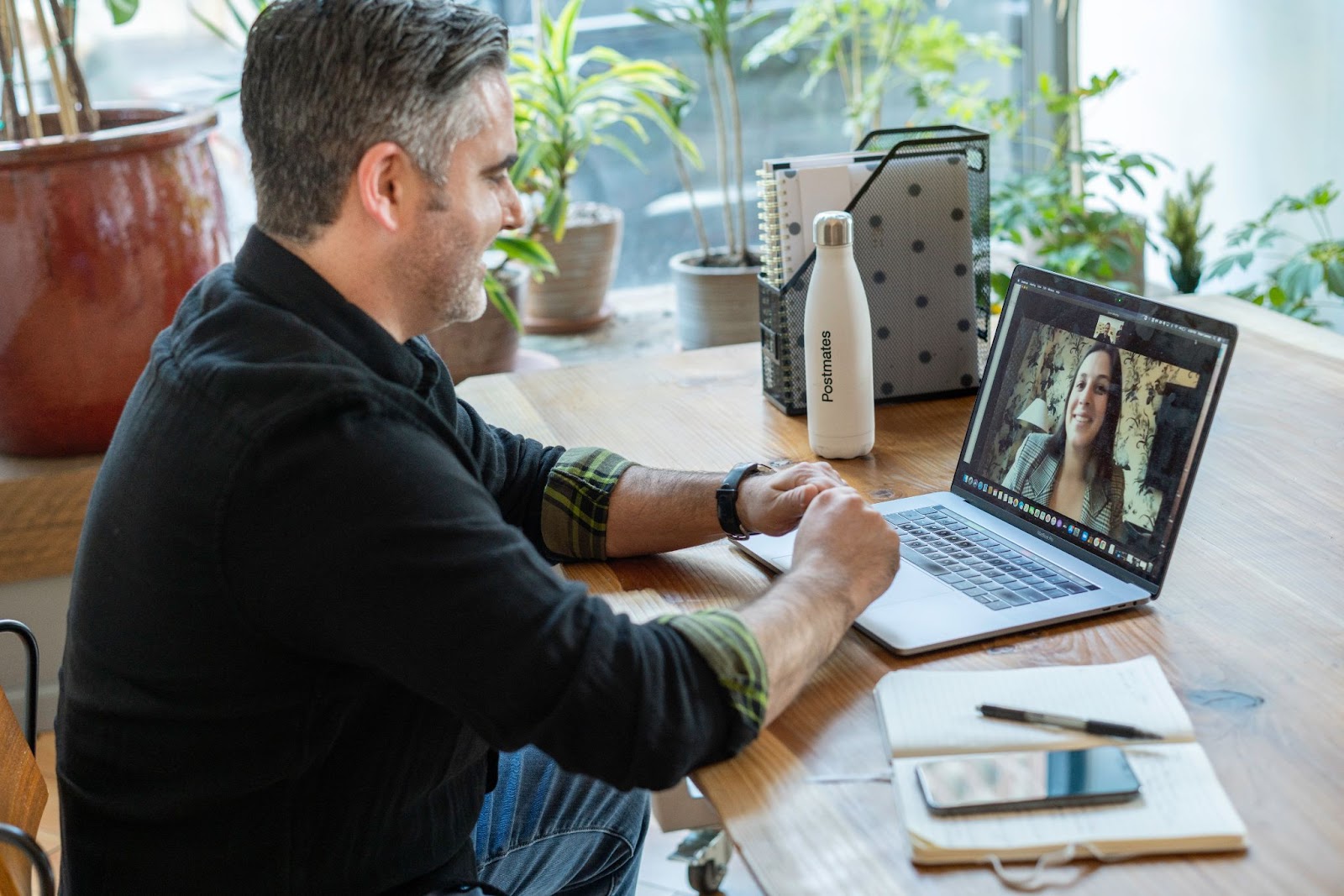 A man and a woman on a video call. Man is at desk, woman is on laptop computer screen that man is looking at. 