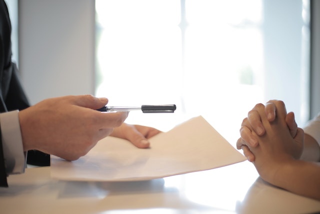 Two people's hands across a desk, one of them is holding a document and pen