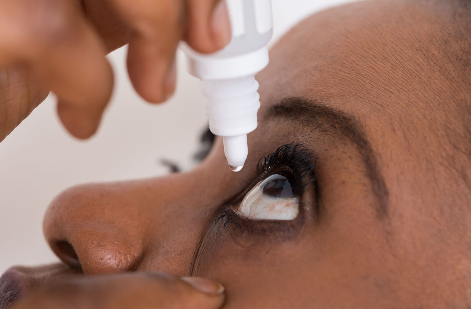 A close-up of a woman using artificial eyedrops on her left eye.