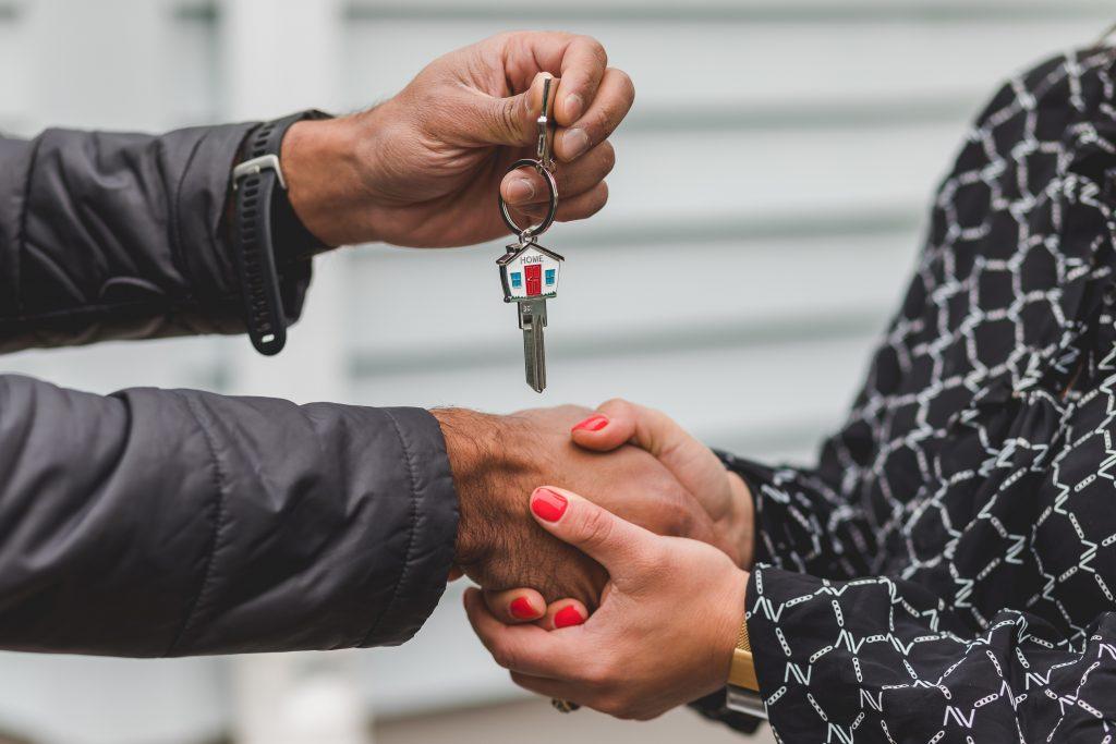 Close up picture of one person giving a key with a house-shaped key chain to another