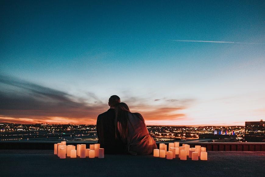 A person and person sitting on a ledge overlooking a city at sunset