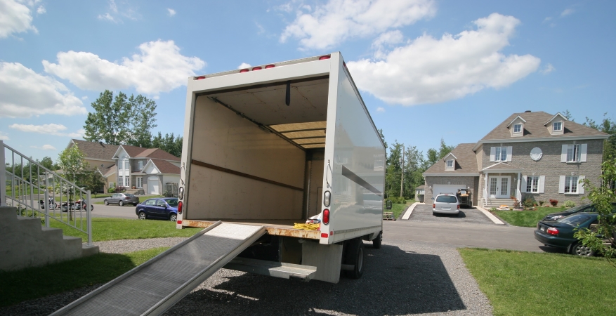 An empty rental truck is backed into a driveway, and the loading ramp is fully extended — signaling it’s ready to be loaded!