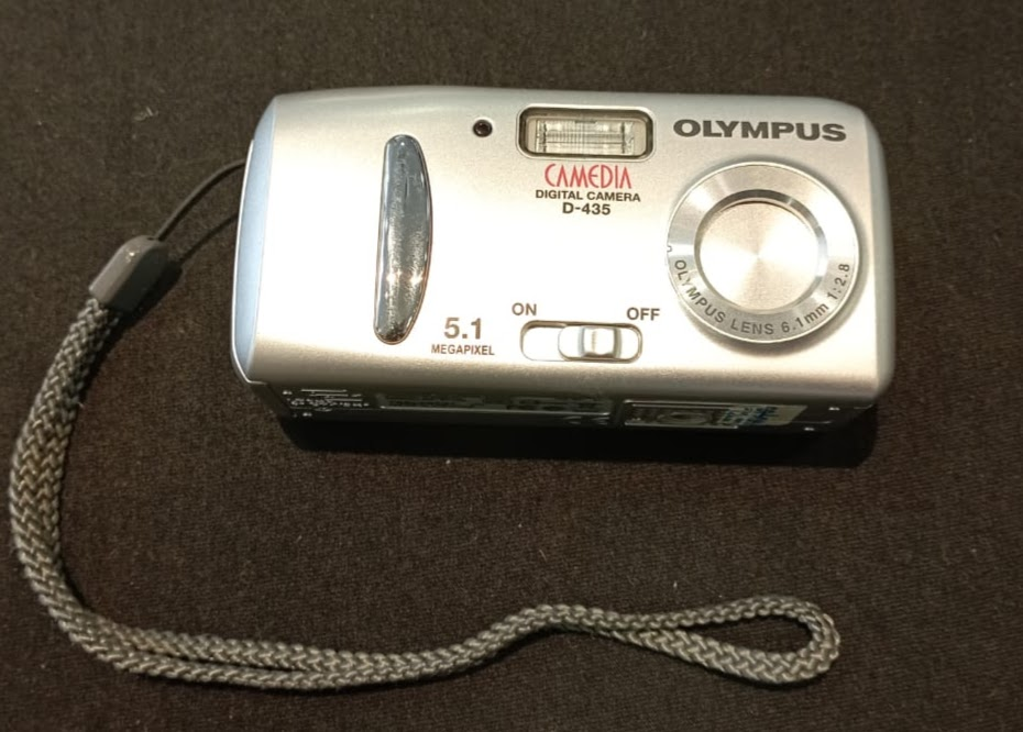 Máquina fotográfica digital, modelo Camedia D-435, marca OLYMPUS. A peça foi utilizada pela seção de Mandados Judiciais até o ano de 2011, adquirida em 2006.