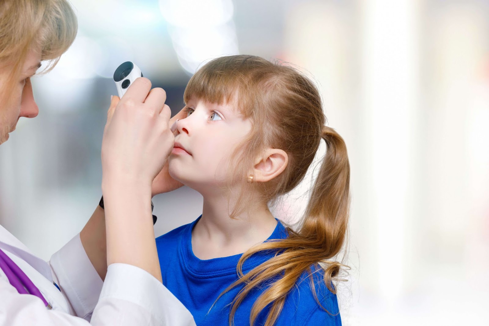 A child facing her optometrist as she shines a small flashlight into her eye.
