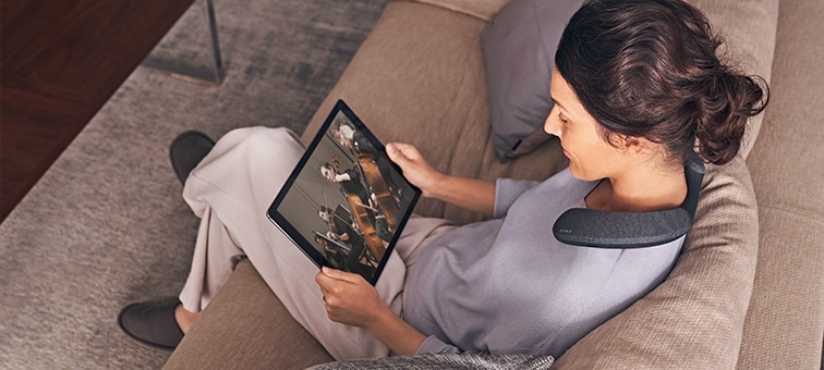 Woman sitting on sofa watching film on tablet using SRS-NS7 wearable speaker