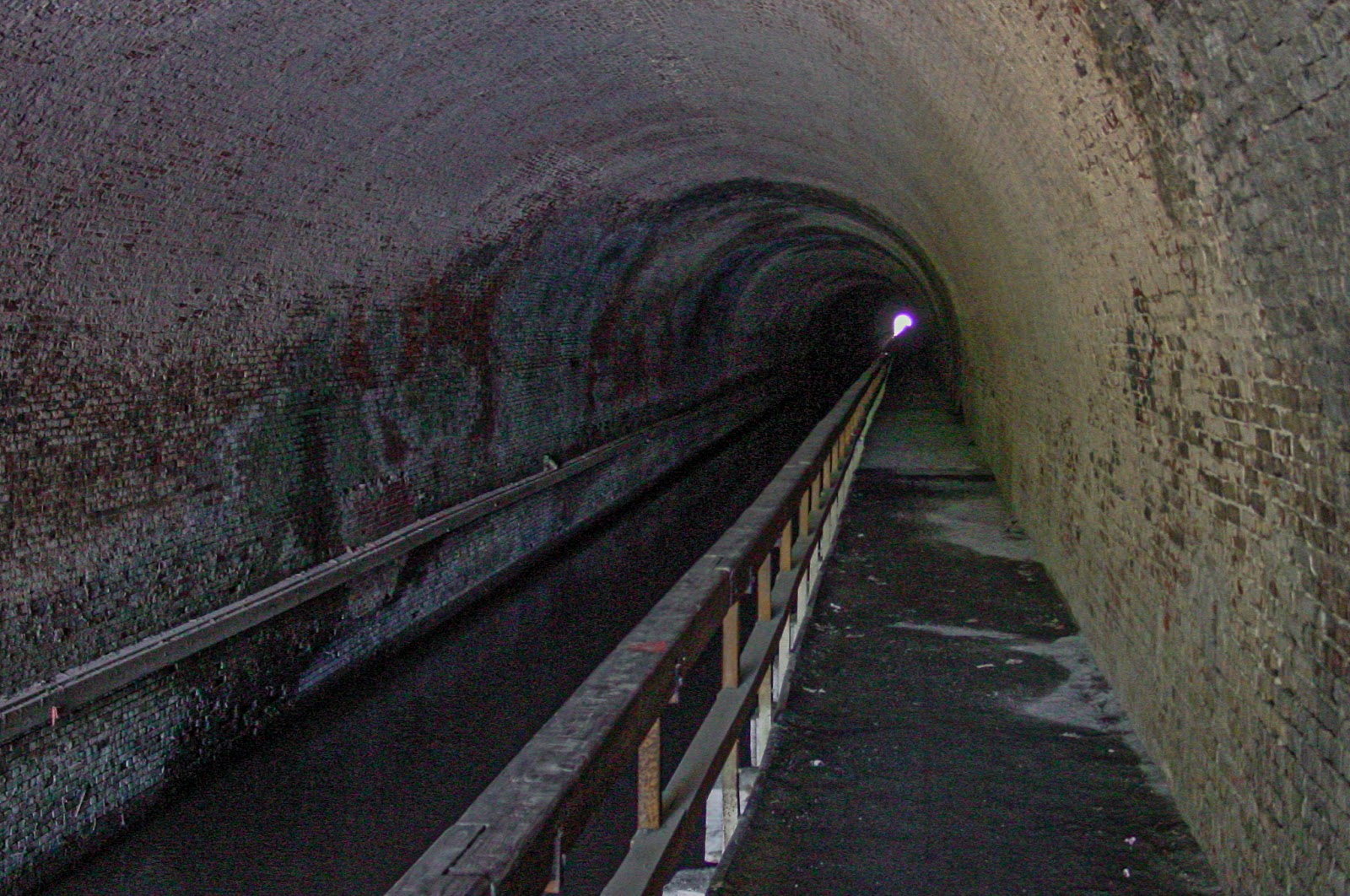 Inside a tunnel, brick interior with boardwalk on right. 