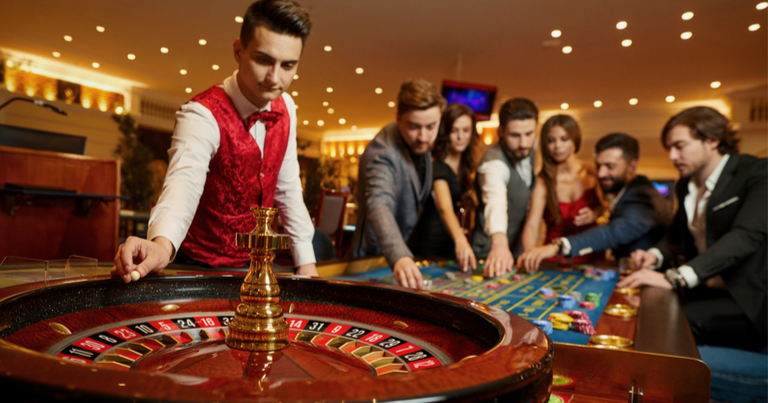 Dealer berdiri di dekat meja dengan roda roulette.