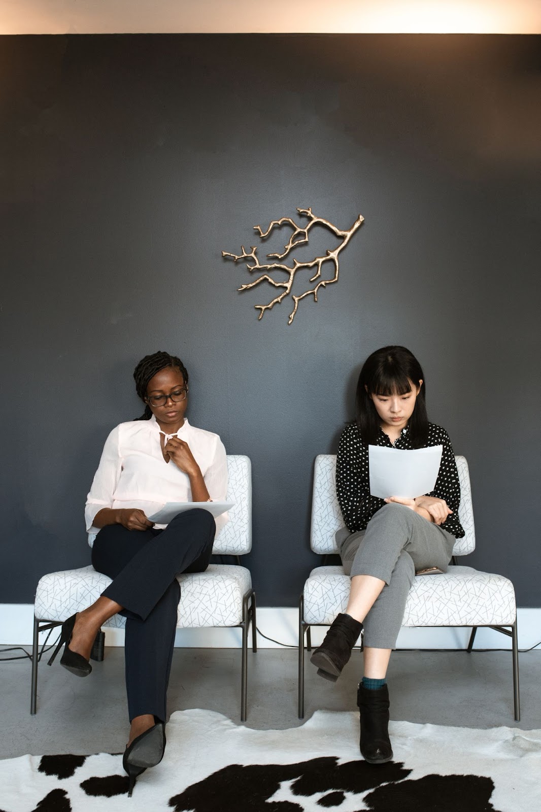 Two women sitting in a lobby, examining their resumes and waiting for their job interview to start