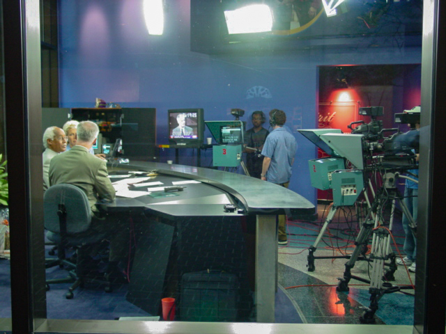 Brightly lit room with cameras pointing at people at a desk.