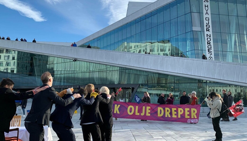 Rebels in suits do a conga in a forecourt outside the opera house. An XR banner hangs down the building.