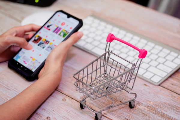 shopping-cart-wooden-table-woman-using-blurry-smartphone-online-shopping