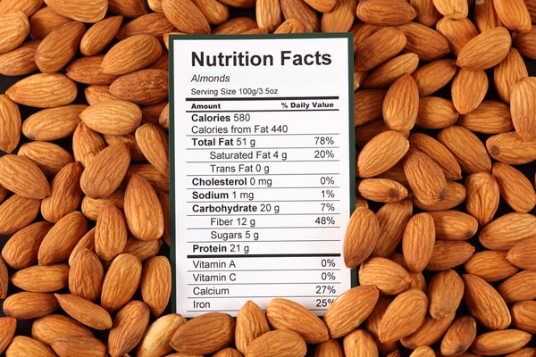 Nutrition label of almonds surrounded by actual almond nuts