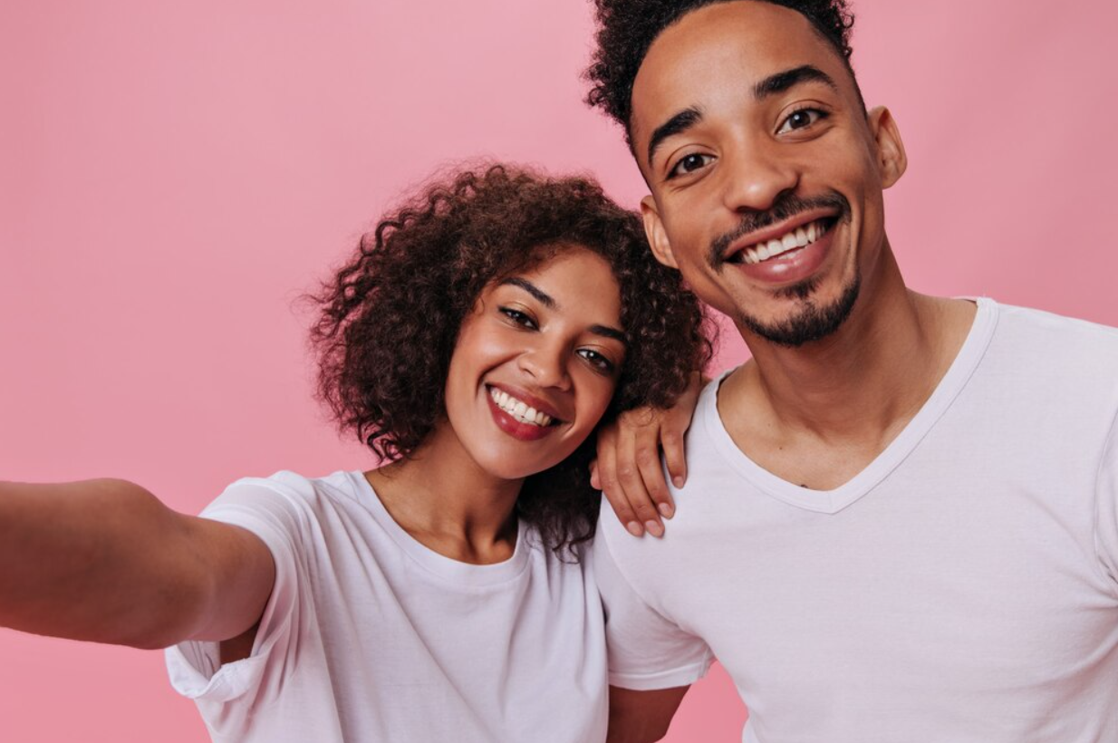 Happy couple in white t-shirts taking selfie on pink wall