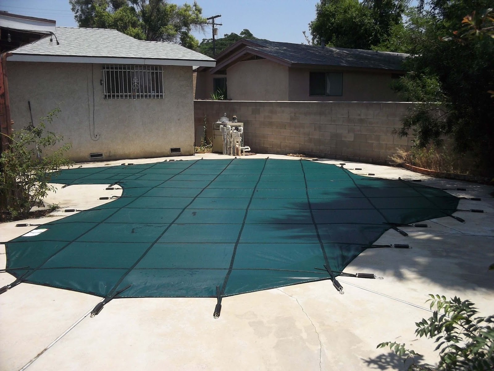 Green mesh pool cover tightly secured above an in-ground pool