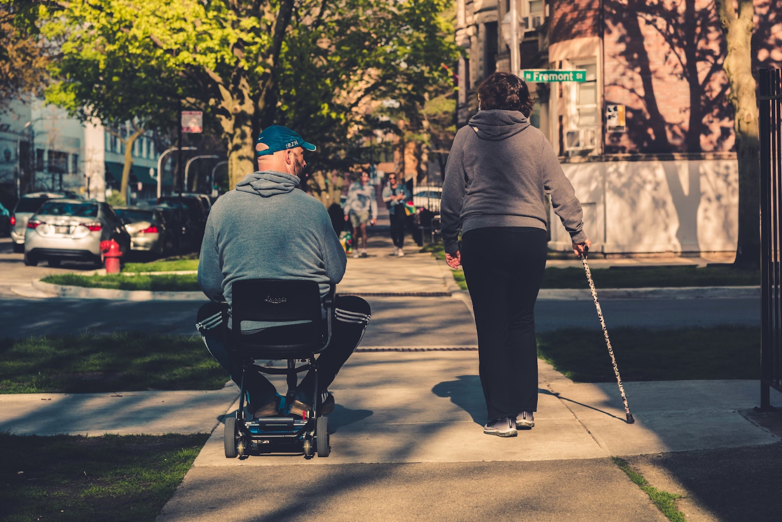 A man in an electric wheelchair and a woman walking with a cane 