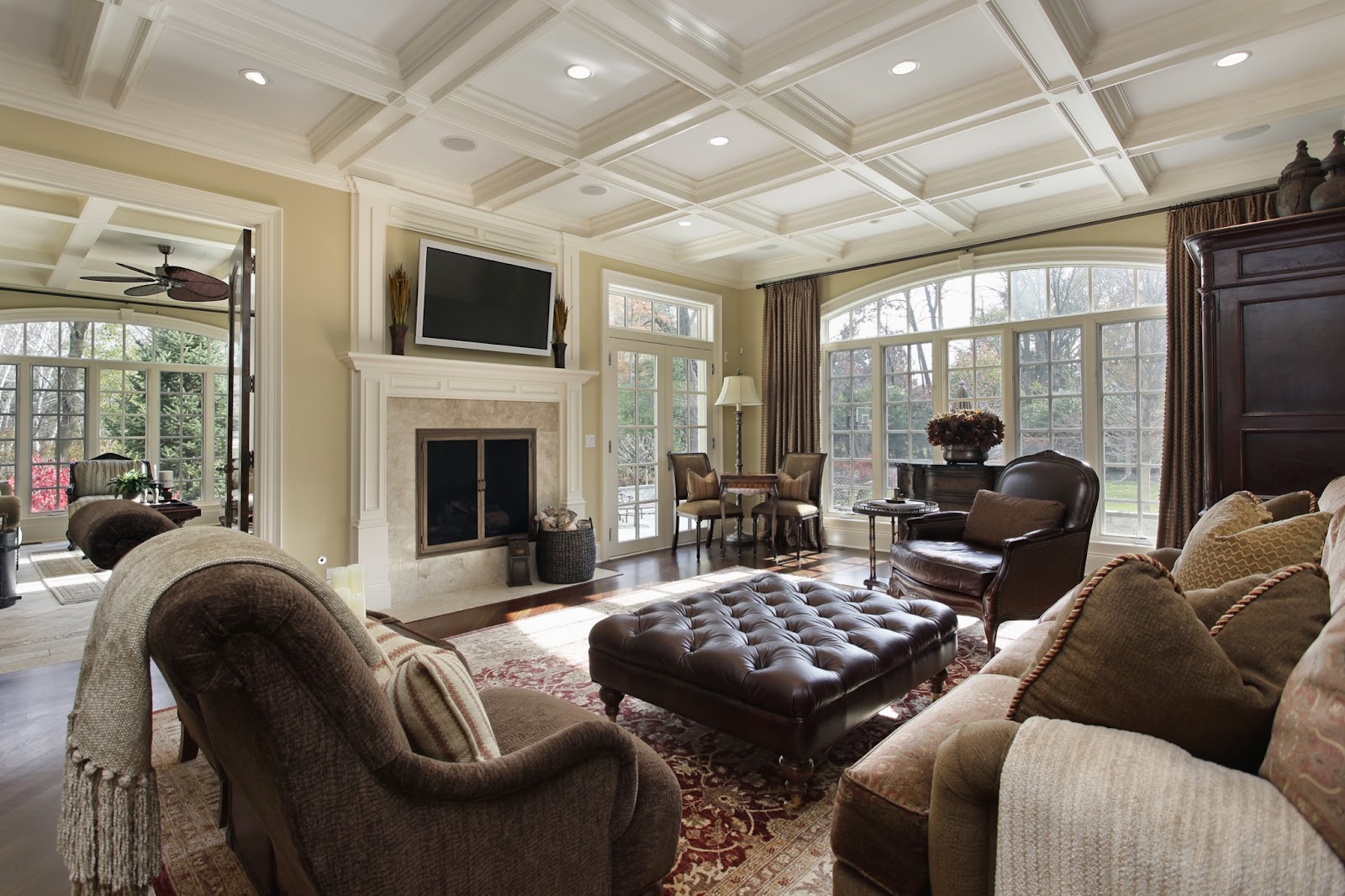 Traditional living room with warm woods, leather accents, large floor to ceiling windows & drapes , coffered ceiling, marble surround and wood fireplace.