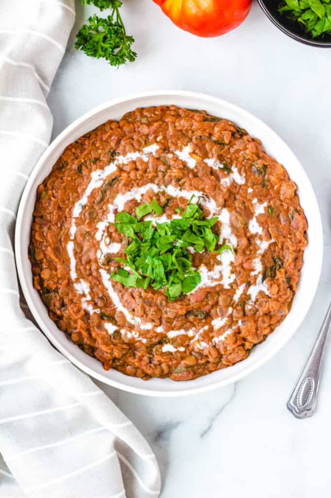Top view of instant pot vegan dal makhani recipe, served in a white bowl with fresh herbs on top.
