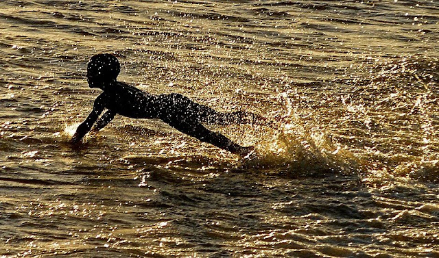 A  fotografia mostra um garoto negro mergulhando em uma praia de Salvador, (BA).