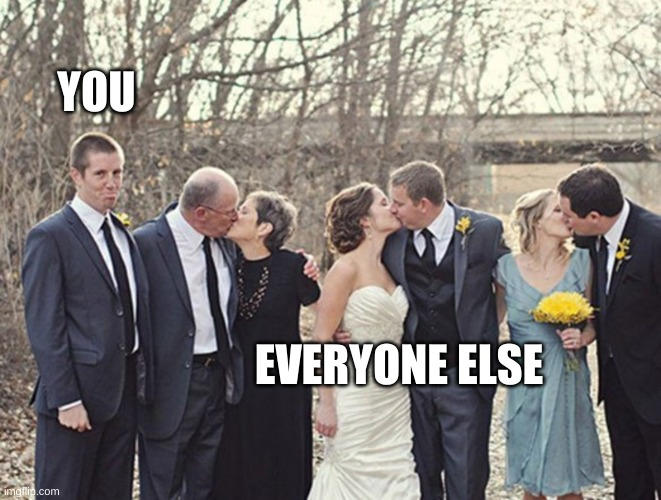 Three couples dressed for a wedding kissing with one man looking sad in the corner by himself.