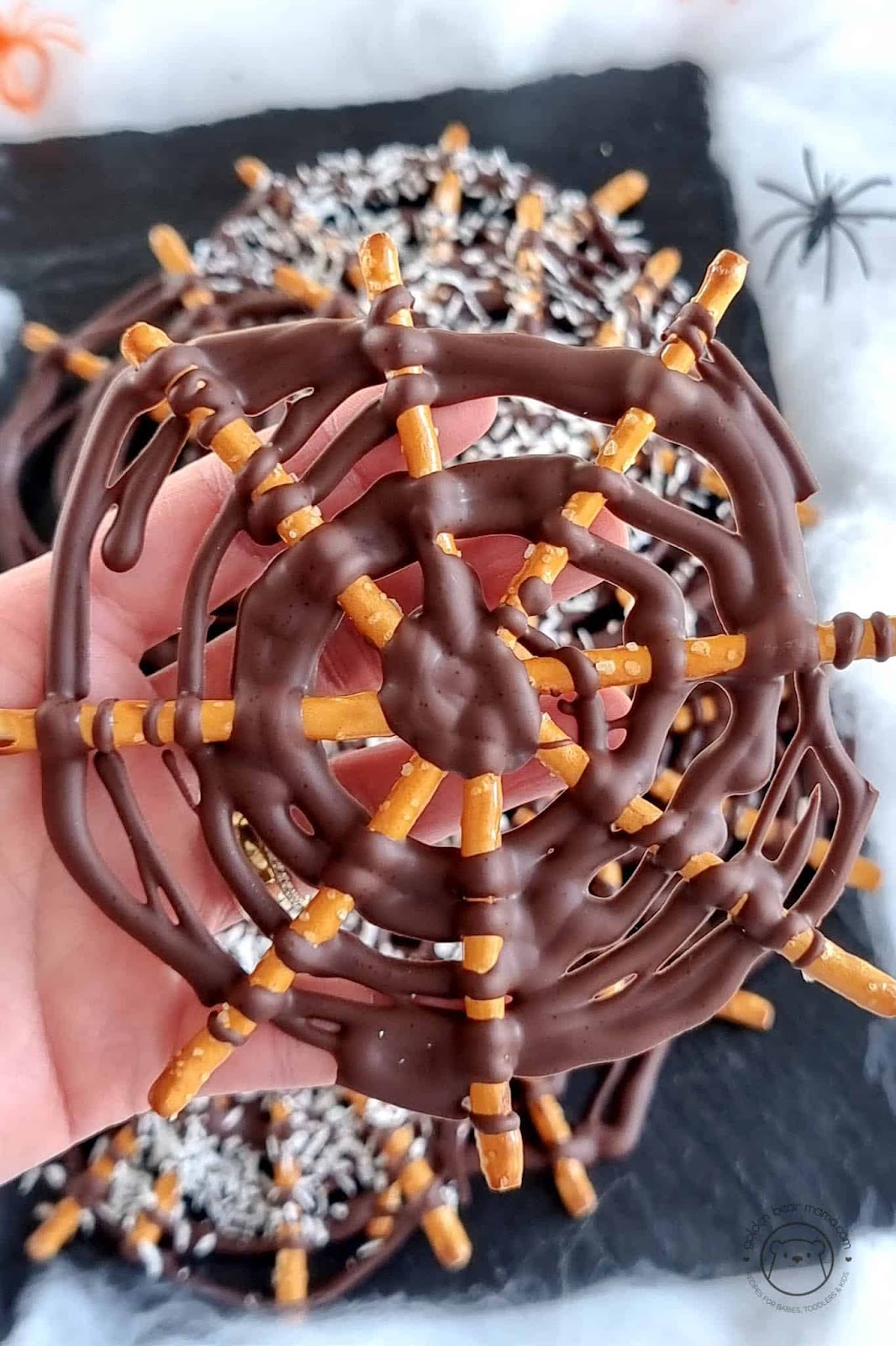 Chocolate spider webs - healthy Halloween treats - made with melted chocolate and pretzels - shown with a hand holding one up.