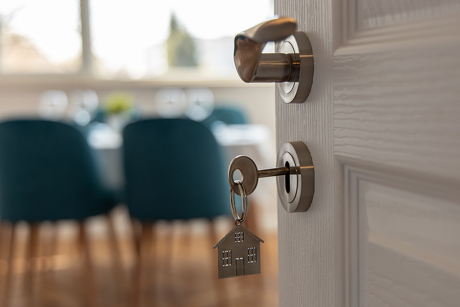 Close up of a key in a closing door with a faded home office behind it. 