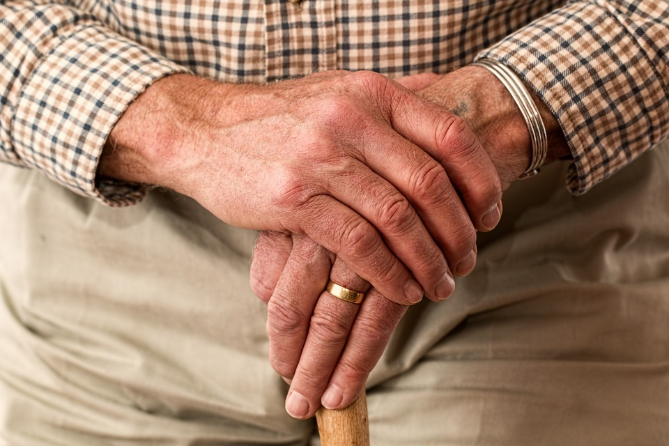 Seated old man's hands on a walking stick