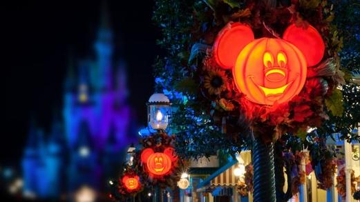 Halloween pumpkin decorations depicting the face of Mickey Mouse adorn light poles on Main Street U S A, with Cinderella Castle in the background