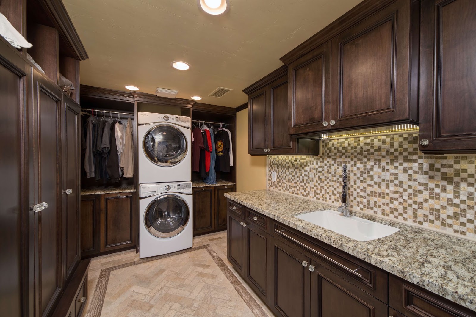 A functional laundry room with stackable washer dryer, countertops and tile backsplash.