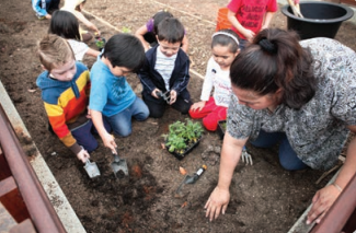 A group of children and their instructor digging in a playground 