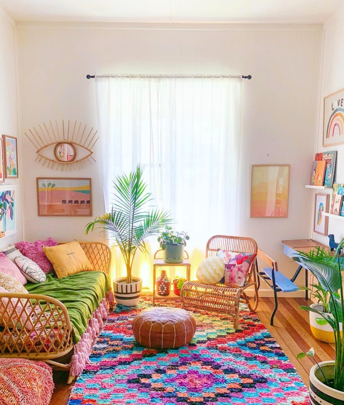 Modern boho living room with a colourful patterned rug, bamboo furniture, and lots of colourful art on the walls