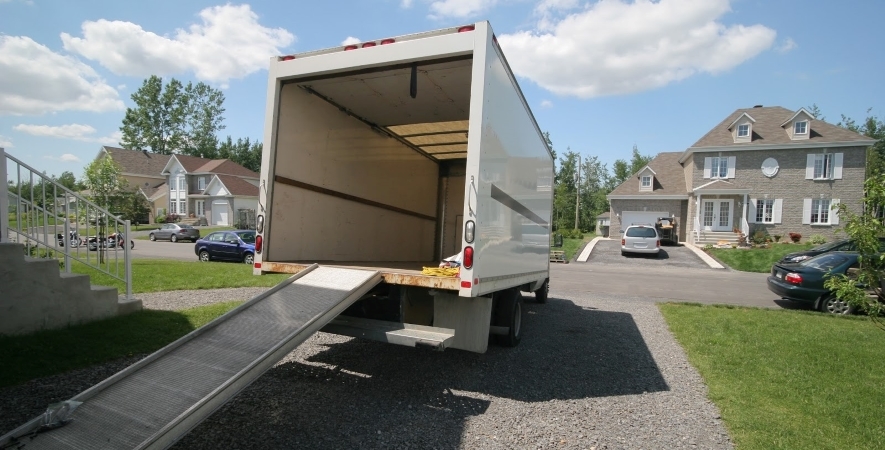 An empty rental truck is sitting in a driveway with its ramp fully extended, ready to be loaded up for a move.