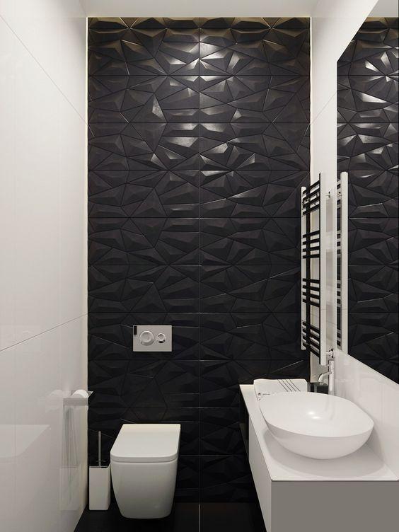 Banheiro com parede principal com revestimento preto em 3D, demais azulejos branco, piso preto, bancada da pia e acessórios brancos.