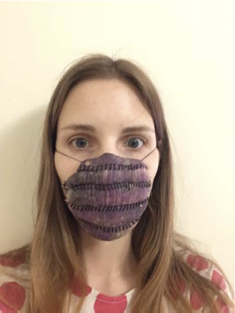 Part of three photographs of a white woman with long dark blonde hair, wearing clothes with large pink dots and her own Personal Protective Purple Daikon Equipment. The text above mentioned proudness, but she mainly looks tired. Her Personal Protective Purple Daikon Equipment covers her face from her nose to her chin. This photo she is facing the camera.