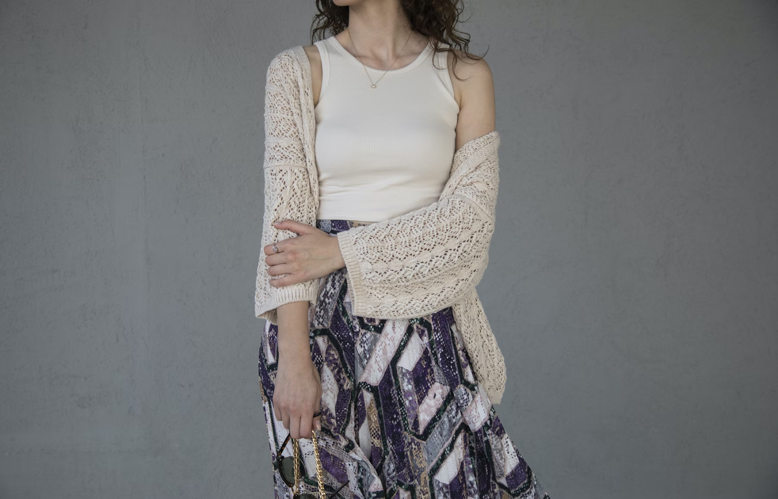 layer without looking bulky: a woman wearing an off white tank top with a crocheted cardigan and dark color patterned pants with geometric shapes