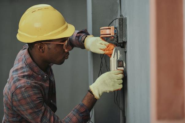 An electrician in a yellow hard hat repairing a fuse box.