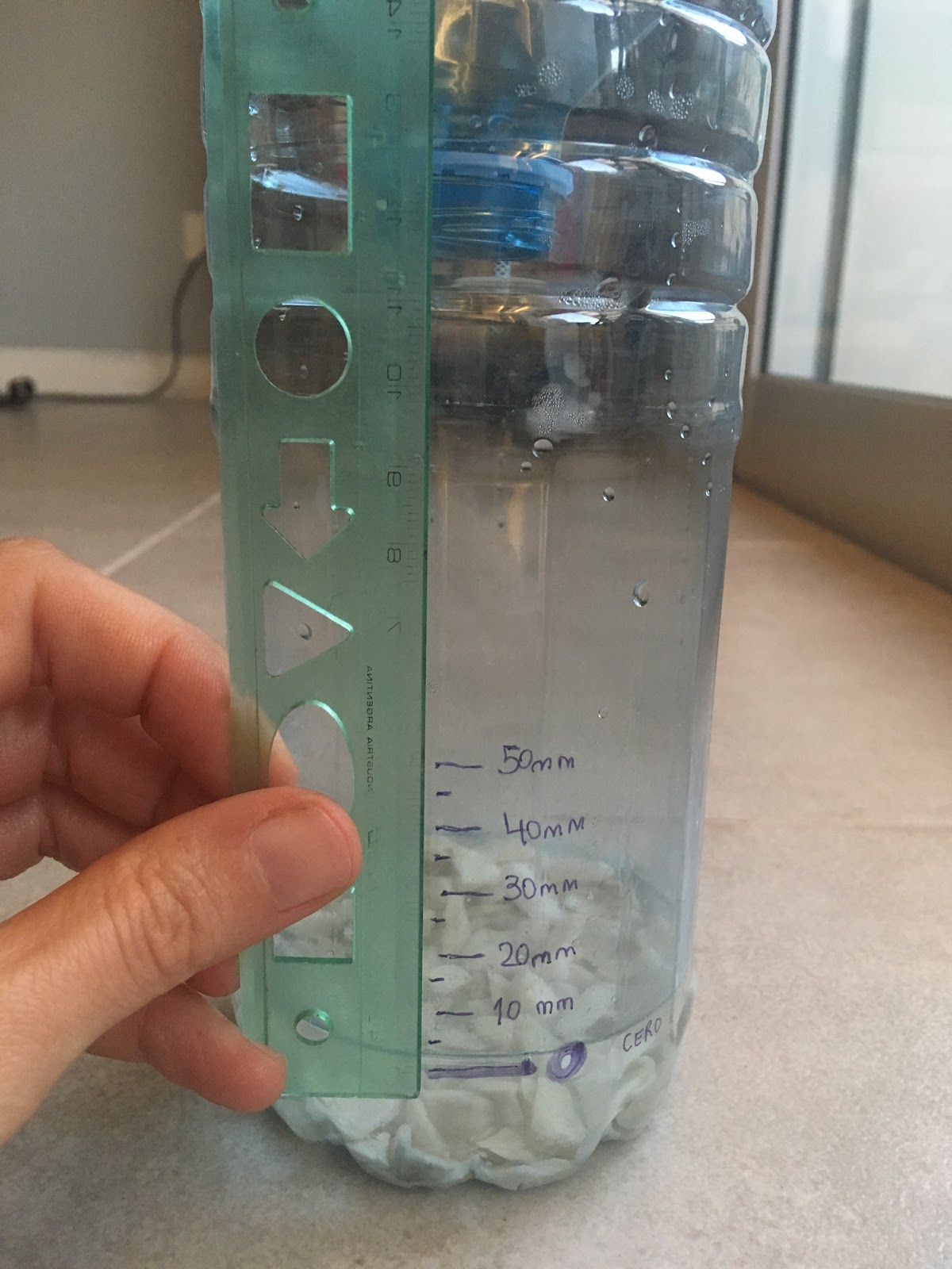 Una botella de plástico cortada con piedras y agua en su interior, marcada con un marcador desde la superficie del agua hacia arriba cada 5 mm.