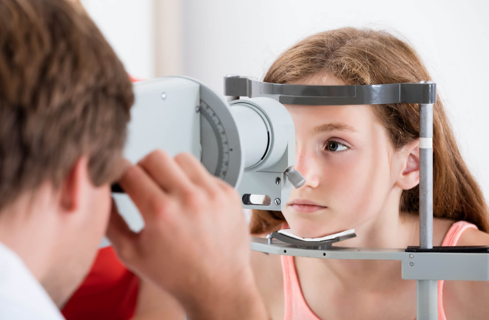 An optometrist smiling and conducting an eye exam on a child using a device that tests her vision.