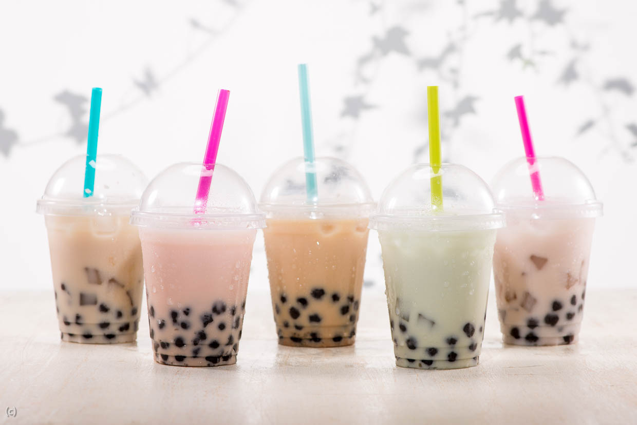 Low angle shot of 5 plastic cups with bobal milk tea in them. They have different colored straws in them.