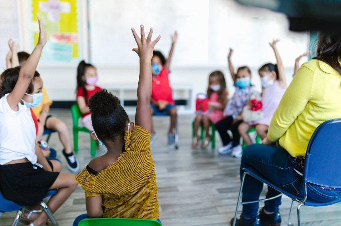 A group of children raising their hands

