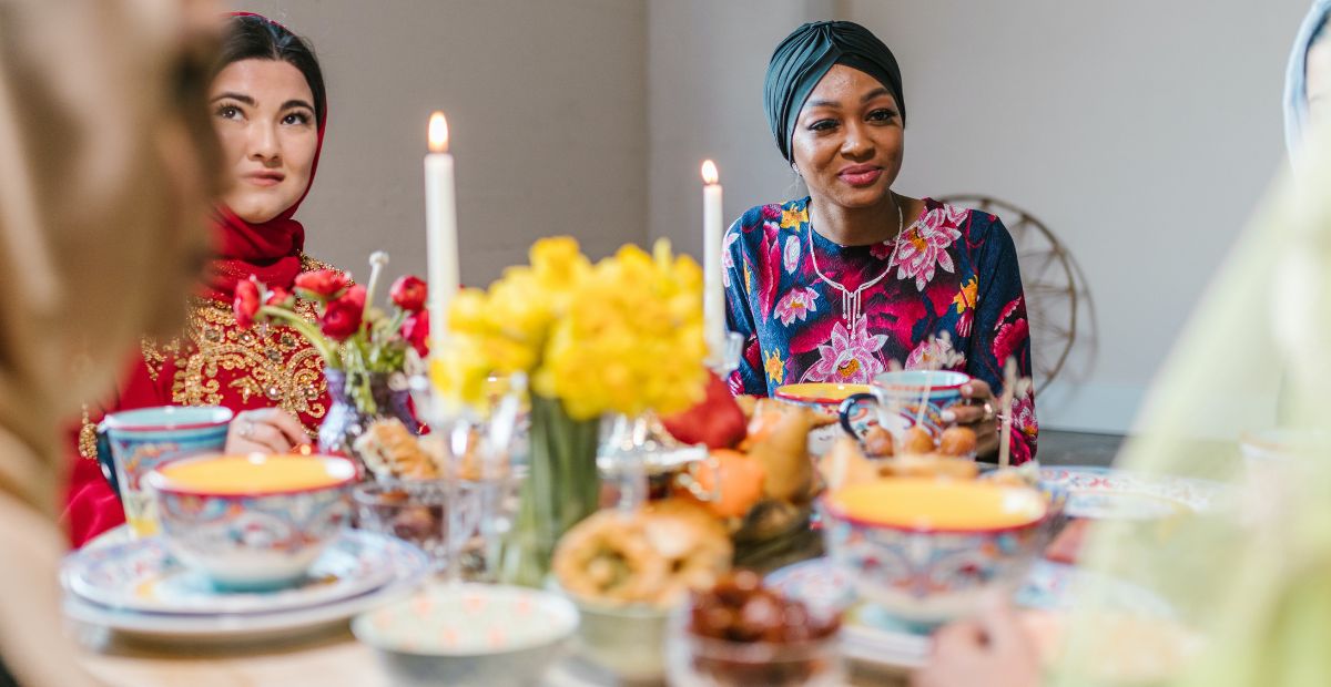 Happy Muslim women at Eid al-Fitr seated at table with delicious meals before them celebrating the end of the Ramadan fast period