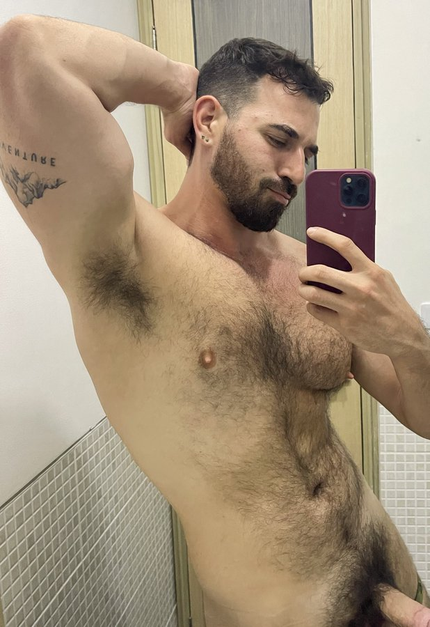 Thick Macho smirking for the camera while flexing his arm naked at the gym and his erect cock visible in the frame