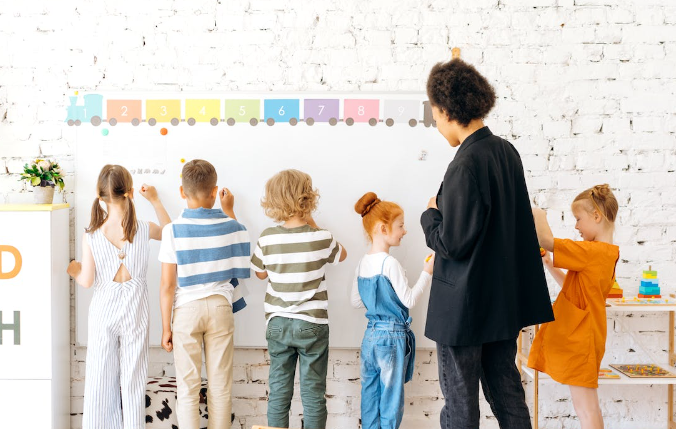 A group of children standing in front of a white board

