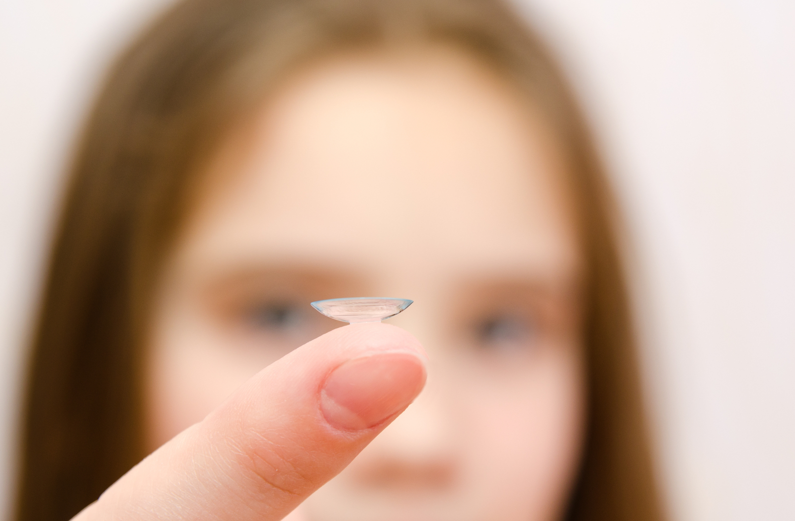 Child with long hair out of focus holding a contact lens for myopia control in focus on her pointer finger