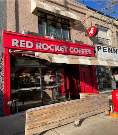 A store front sign that says "Red Rocket Coffee", the sign is red with grey letters and there is a window.