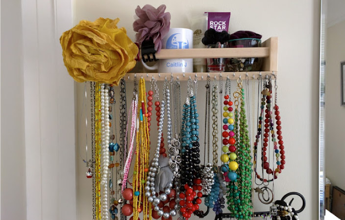 An IKEA spice rack, repurposed as a necklace organizer. It's covered in colorful necklaces. 