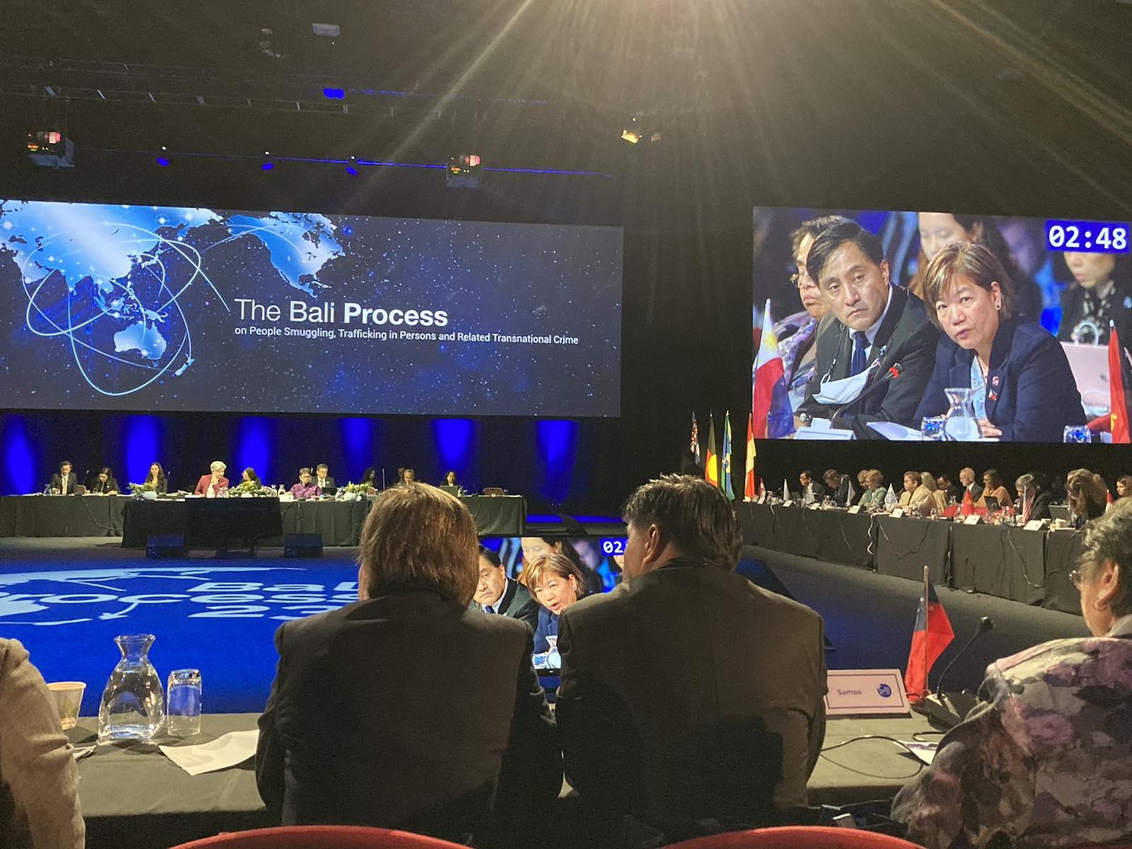 A group of people sitting at a table with a large screen behind them

Description automatically generated with low confidence